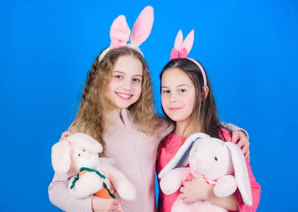 Sisters glimlachen schattige Bunny kostuums. Verspreid vreugde en geluk rond. Hoop liefde en vreugdevolle leven. Vrienden kleine meisjes met bunny oren vieren Pasen. Kinderen met Bunny Toys op blauwe achtergrond — Stockfoto