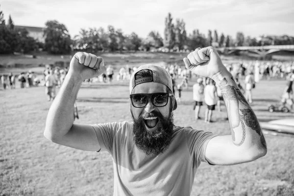 Fã alegre no festival de verão. Homem hipster barbudo na frente da multidão as pessoas levantam punhos fundo ribeirinha verde. Celebração de eventos urbanos. Hipster em cap feliz comemorar festa de piquenique evento ou festival — Fotografia de Stock