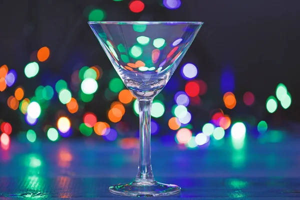 Cocktail glass on defocused garland colorful lights. What to drink on christmas party. Alcohol cocktail for winter party. Cocktail ideas concept. Easy recipes for winter alcoholic cocktail drinks