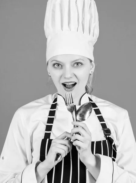 Im a great cook. Sensual lady cook. Pretty cook holding stainless steel spoon and fork. Professional woman cook wearing traditional white chef hat and apron