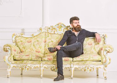Hipster kibirli yüzünde yalnız oturuyor. Sakallı ve bıyıklı lüks oturma odasında boş zaman harcıyor. Zengin ve yalnız kavramı. Lüks daire sahibi beyaz duvar arka koltukta oturur