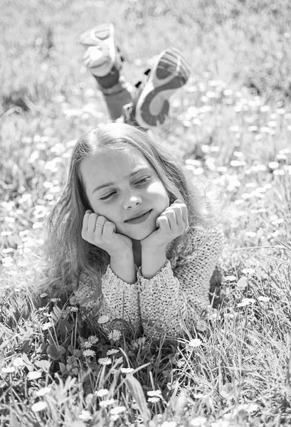 Mädchen liegt auf Gras auf Grasfläche, grüner Hintergrund. Kinder genießen frühlingshaftes sonniges Wetter auf der Wiese. Mädchen mit verträumtem Gesicht verbringen ihre Freizeit im Freien. Blütezeit-Konzept — Stockfoto