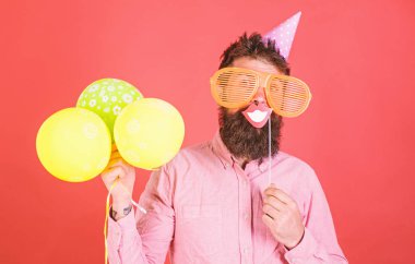 Hava balonları ile parti şapkalı adamı kutluyor. Hippi dev güneş gözlüğü kutluyor. Neşeli yüzündeki sakallı gülümseyen ağız sopa, kırmızı bir arka plan üzerinde tutar. Fotoğraf booth eğlence kavramı