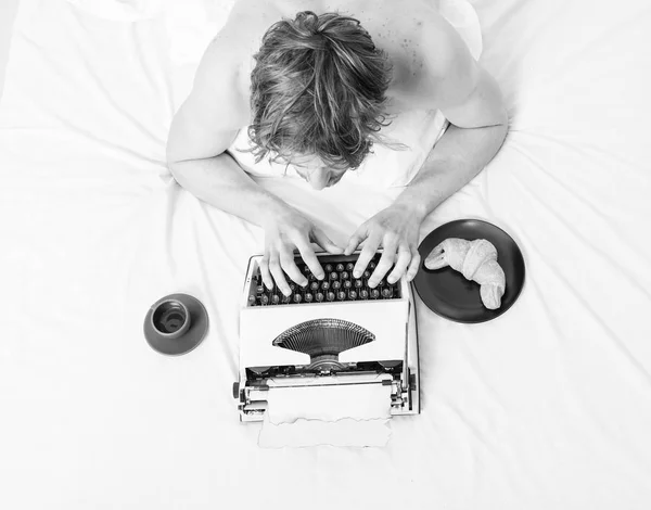 Autore ragazzo tousled capelli occupato scrivere capitolo scadenza venuta vista dall'alto. Uomo ispirato laici biancheria da letto libro di lavoro. Scrittore autore usato vecchia macchina da scrivere. Uomo con macchina da scrivere e caffè giaceva letto — Foto Stock