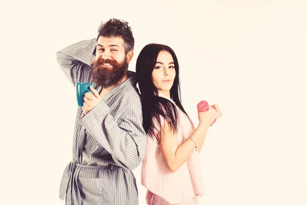 Adorable couple standing back to back while holding cup of coffee and dumbbell. Morning routine concept. Couple full of energy after morning exercises and coffee, copy space