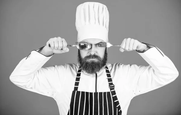 Kocken allvarligt strikt ansikte håll sked och gaffel. Matlagning processen koncept. Kan prova maträtt. Hungriga kock redo att prova mat. Dags att prova smak. Man stilig med skägg innehar köksutrustning på blå bakgrund — Stockfoto