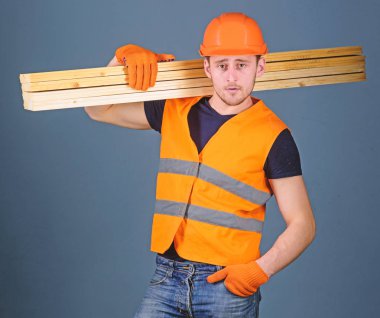 Marangoz, woodworker, işçi, Oluşturucu emin yüz taşıdığı ahşap kirişler omuz üzerinde. Hardy işçi kavramı. Adam kask, kask ve koruyucu eldiven tutan ahşap kiriş, gri arka plan