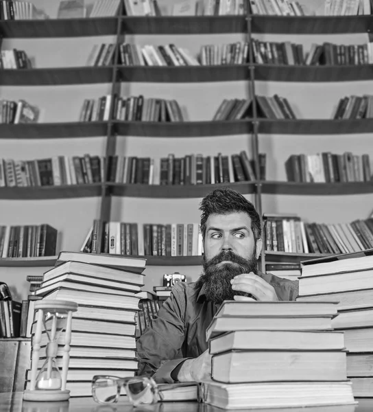 Öğretmen ya da öğrenci sakallı kum saati ve gözlük, defocused ile masaya otur. Kitap kurdu kavramı. Katı yüz sit Kitaplığı'nda, eğitim sırasında kitaplar, kitap rafı arka plan üzerinde yığınları arasında adam