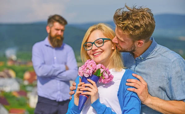 Couple in love dating while jealous bearded man watching wife cheating him with lover. Lovers hugs outdoor flirt romance relations. Infidelity concept. Couple romantic date lovers bouquet flowers — Stock Photo, Image