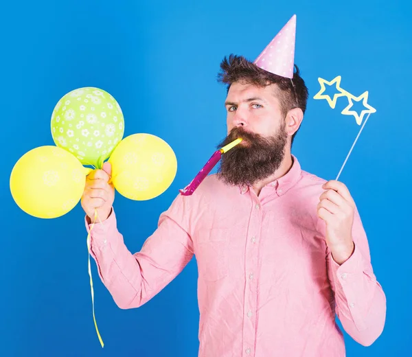 Entertainer with colorful baloons at kids party, international childrens day. Bearded artist with party wistle and paper star shaped glasses wearing birthday cap. Bearded man on blue background