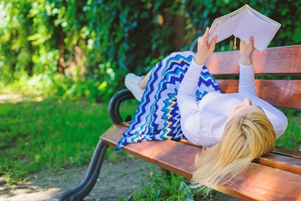 Дівчина лежала в парку, розслабляючись з книгою, зеленим фоном природи. Жінка проводить дозвілля з книгою. Цікава книжка. Розумний і гарний. Дівчина читає на відкритому повітрі, розслабляючись на лавці. Розумна леді розслабляється — стокове фото