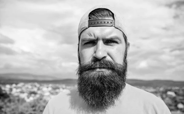 Elegante casual. Un hipster genial. Barbudo hombre en la moda hipster cap al aire libre. Un hombre brutal con barba larga y bigote. Hipster en ropa de moda callejera en el paisaje de verano —  Fotos de Stock