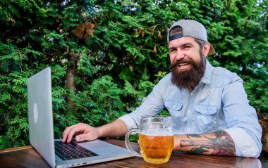 Sonunda Cuma. Hipster rahat açık havada bira ile oturma teras. Sakallı hipster Freelancer bira kupa ile çalışma günün sonu zevk. Bu bardağı hak ediyor. Bira ve online oyun ile acımasız adam eğlence