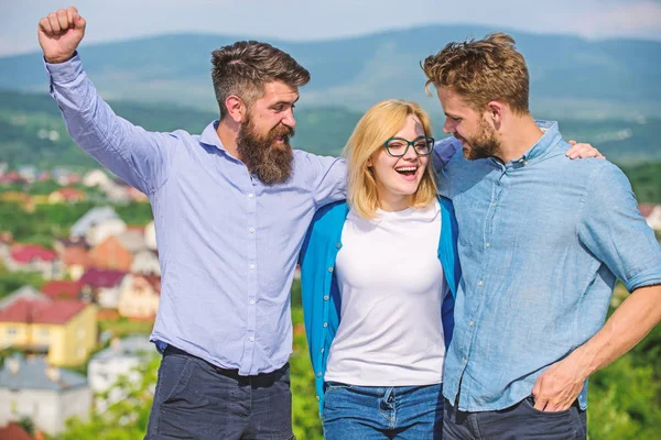 Company reached top. Business team concept. Men with beard in formal shirts and blonde in eyeglasses as successful team. Company of three happy colleagues or partners hugs outdoor, nature background