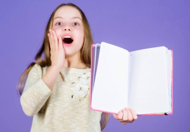 Kütüphanedeki sınavlara hazırlanıyorum. Küçük mutlu çocuk açık bir kütüphane kitabı tutuyor. Kitapla gülümseyen sevimli küçük kütüphane okuyucusu. Okul kütüphanesinde okumak, kopyalama alanı