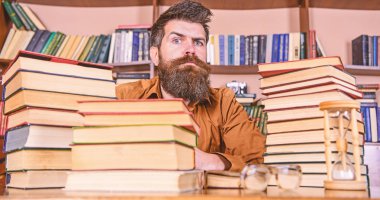 Katı yüz sit Kitaplığı'nda, eğitim sırasında kitaplar, kitap rafı arka plan üzerinde yığınları arasında adam. Öğretmen ya da öğrenci sakallı kum saati ve gözlük, defocused ile masaya otur. Kitap kurdu kavramı