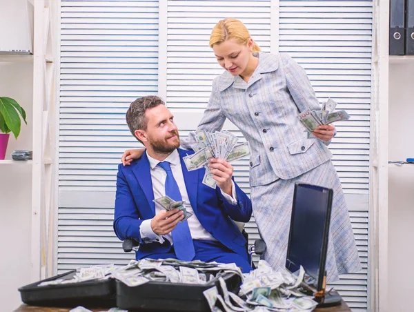 Excited successful businessman opened a box with money and rejoices in profits. Happy young businessman in suit throwing money up while sitting near case full of paper currency.