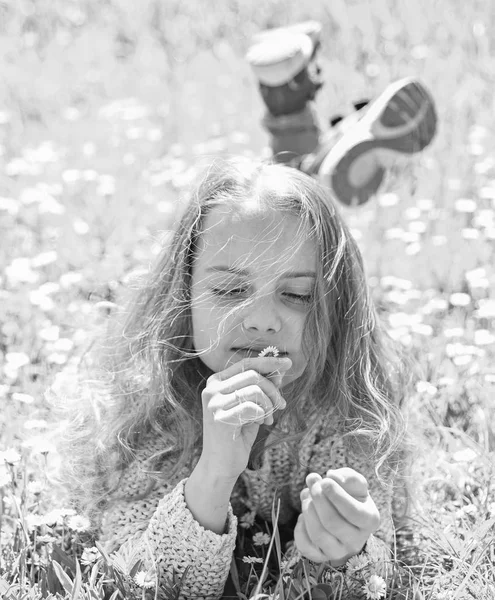 Mädchen auf Gras liegend, Graspflanze im Hintergrund. Mädchen mit verträumtem Gesicht hält Gänseblümchenblümchen in der Hand. Kinder genießen das sonnige Frühlingswetter auf einer Wiese mit zarten Gänseblümchen-Blüten. Sensibilitätskonzept — Stockfoto