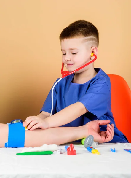 Gezondheidszorg. Kid kleine arts zitten tafel met stethoscoop en medische hulpmiddelen. Geneeskunde concept. Meten van de bloeddruk. Medisch onderzoek. Medische educatie. Jongen schattig kind toekomstige arts carrière — Stockfoto