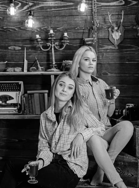 Rahatlatıcı ve mulled şarap içme kızlar. Arkadaşlar rahat kıyafetler içinde sıcak atmosferi, ahşap iç tadını çıkarın. Tatil ve tatil kavramı. Gülümseyen yüzler kareli giysiler rahatlatıcı arkadaşlar