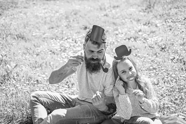 Aristocrates koncept. Familjen tillbringar fritid utomhus. Pappa och dotter sitter på gräset på grassplot, grön bakgrund. Barn och far poserar med hög hatt, läppar och röret foto monter attribut — Stockfoto