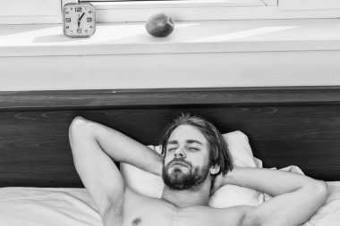 Yatakta uyanma ve kollarını uzanan bir delikanlı. Ayakları rahat yatakta uyuyan adamın. Adam el tatile çalar saat için uzanarak battaniyenin altında.