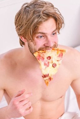 Adam yakışıklı bekar yatakta kahvaltı için peynirli yemek yeme sakallı. Yakışıklı adam bir parça pizza elinde tutar ve bu yemek. Hafta sonu.