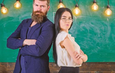 Sakal ve gözlük stand sırt sırta, kara tahta arka plan öğretmen olan adam. Öğretmen ve öğretmen rahat görünüyor. Okul personeli kavramı. Bayan ve birlikte okulda çalışan hipster