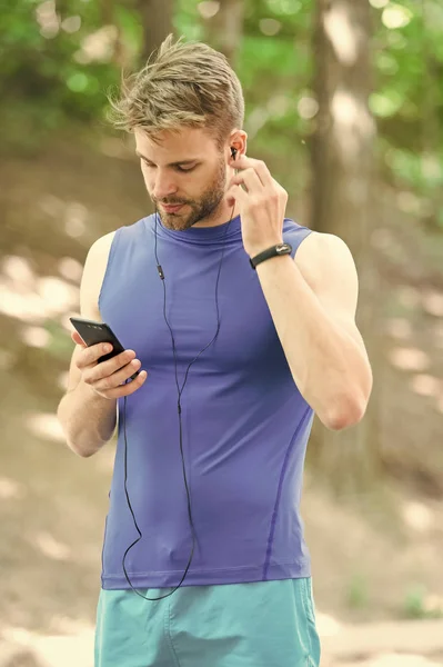 Music best companion to run. Man athlete on busy face set up play list, nature background. Sportsman training headphones listen music. Athlete with bristle with fitness tracker or pedometer