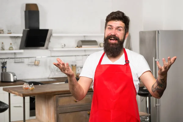 Cocinar en cocina nueva. Necesito inspiración culinaria. El fin de semana comienza con un delicioso desayuno. Cómo convertir la cocina en casa en hábito. Hombre barbudo delantal hipster rojo de pie en la cocina. Tienda de muebles de cocina —  Fotos de Stock