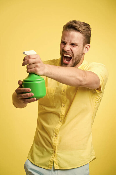 Мачо держать пластиковые баллончик спрей как пистолет желтый фон. Парень с водяным спреем в руке притворяется, что стреляет. Концепция домашнего хозяйства и гигиены. Позаботьтесь о увлажнении. Концепция увлажнения
