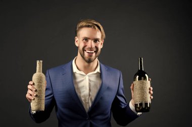 Sommelier 'de iki şişe şarap var. Profesyonel şarap arıtma konsepti. Elinde şarap şişeleri olan resmi takım elbiseli bir adam. Sommelier yakışıklı, esmer arka plandaki neşeli adam. Hangi şarabı seversin?