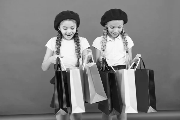 Niños lindas colegialas sostienen manojo bolsas de compras. Niños satisfechos comprando fondo rojo. Obsesionado con centros comerciales y de ropa. Concepto Shopaholic. Compras se convierten en diversión con los mejores amigos —  Fotos de Stock