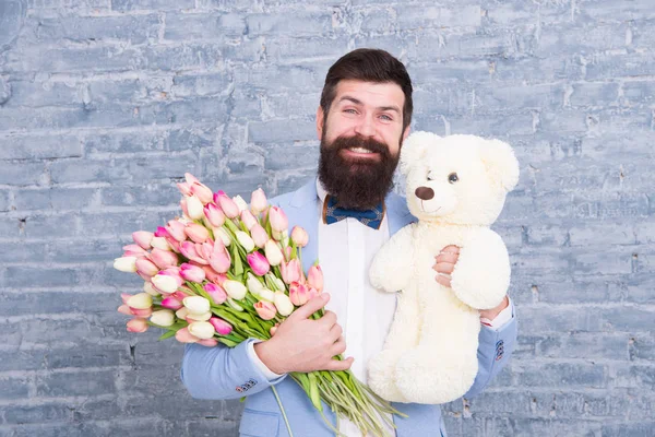 Romantic gift. Macho getting ready romantic date. Man wear blue tuxedo bow tie hold flowers bouquet. International womens day. Surprise will melt her heart. Romantic man with flowers and teddy bear