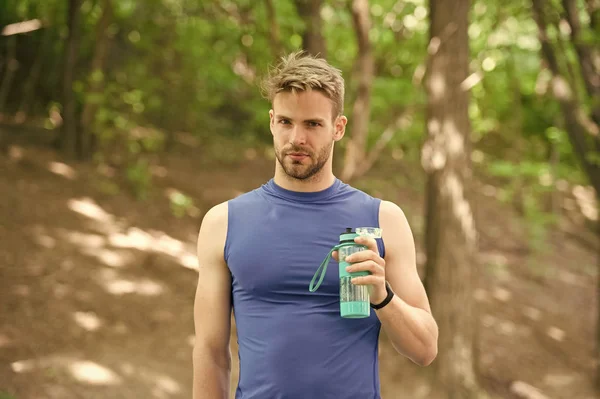 Preparándose para otra actividad. El aspecto atlético del hombre sostiene la botella con agua. El atleta se preocupa por el equilibrio hídrico. Deporte y estilo de vida saludable. Atleta beber agua después de entrenar en el parque — Foto de Stock