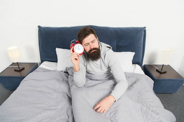 Need more sleep. Get up with alarm clock. Tips for waking up early. Man bearded sleepy face bed with alarm clock in bed. What terrible noise. Turn off that ringing. Problem early morning awakening — Stock Photo, Image