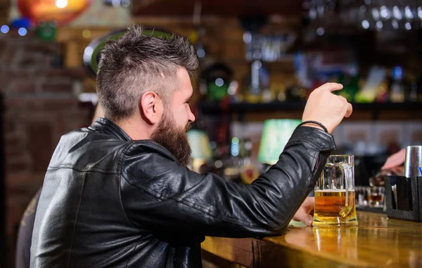 Az ember szakáll költ szabadidő sötét Bar. Hipster pihentető bár, sör. Brutális csípő szakállas férfi ül Bar Counter sört inni. Péntek este. Bár pihentető hely, ahol megihat egy italt és pihenhet — Stock Fotó