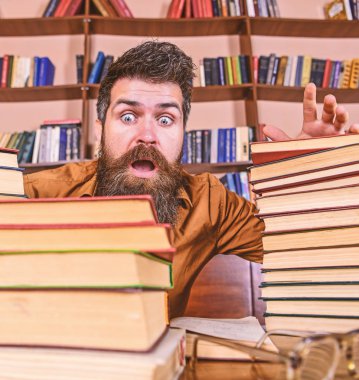 Adam Kitaplığı'nda, eğitim sırasında kitaplar, kitap rafı arka plan üzerinde yığınları arasında şok yüzünde. Son Tarih kavramı. Öğretmen ya da öğrenci sakallı defocused gözlük ile masada oturur