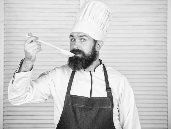 Кулінарія як професійна професія. Хіпстерський бородатий шеф-кухар тримає дерев'яну ложку. Кухонне начиння та концепція приготування їжі. Давайте спробуємо смак. Додайте трохи спецій. Чоловік з бородою в капелюсі і фартух тримає інструменти для приготування їжі — стокове фото