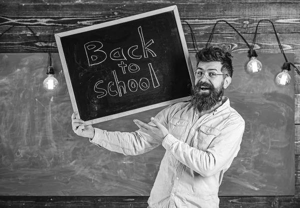 Teacher in eyeglasses holds blackboard with title back to school. Man with beard and mustache on happy face welcomes students, chalkboard on background. High school concept — Stock Photo, Image