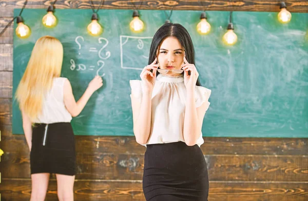 Meisje ziet er aantrekkelijk uit terwijl dame schrijvend op schoolbordachtergrond, ongeconcentreerd. Studenten en stagiairs concept. Leerling, leraar in bril staan in de klas. Aantrekkelijke vrouwen die zich voorbereiden op de les — Stockfoto