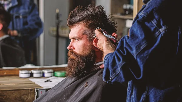Barber with hair clipper works on hairstyle for bearded man barbershop background. Hipster lifestyle concept. Barber styling hair of brutal bearded client with clipper. Hipster client getting haircut — Stock Photo, Image