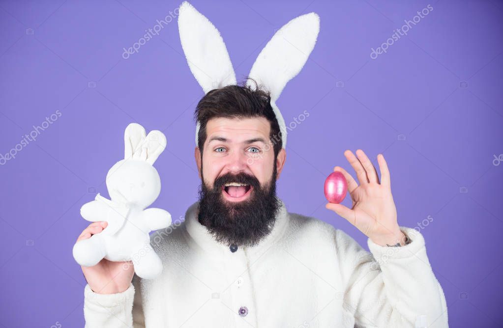 Spring, new life and fertility. Happy man with rabbit ears holding bunny toy and egg. Bearded man in rabbit costume with easter egg and hare toy. Spring holiday celebration. Excited about Easter
