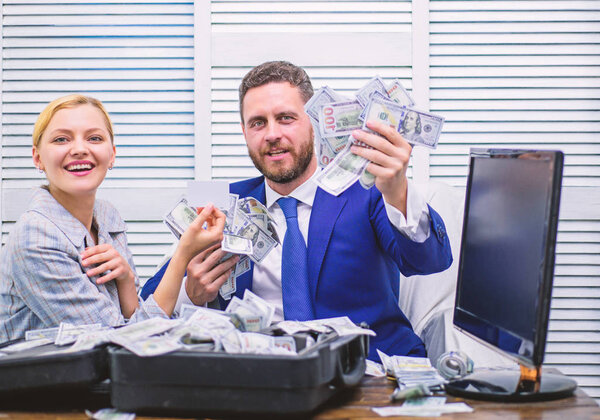 Handsome man happy and surprised with money hundreds dollars in case. Young businessman looking at money scattered on table. Profit and richness concept.