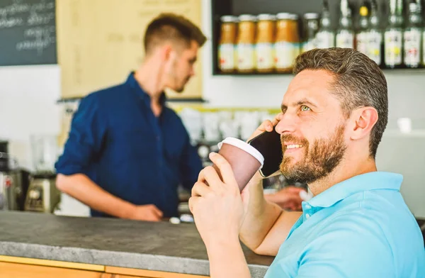 Happy to hear you. Man solving problems phone have coffee. Confident entrepreneur choose drink in paper cup to go while communicate mobile. Man speak mobile phone and drink coffee cafe bar background