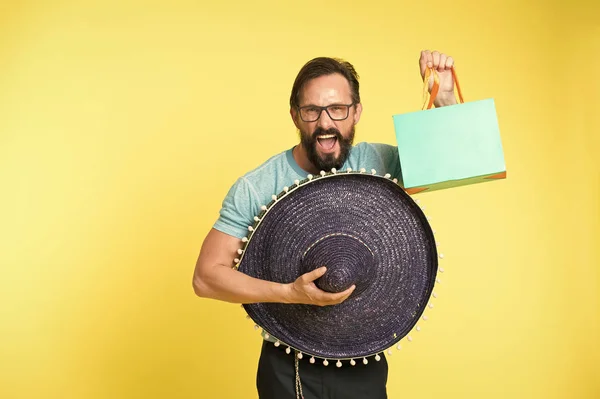 Urlaubs- und Geschenkkonzept. Mann mit fröhlichem Gesicht Sombrero-Hut hält Einkaufstasche gelben Hintergrund. Mann mit Bart und Sombrero. Mann hält Einkaufstasche in der Hand. Saisonverkauf und Rabatt — Stockfoto
