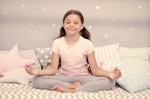 Meditate before go to bed. Girl child sit on bed in her bedroom. Kid prepare to go to bed. Pleasant time for evening meditation. Girl kid long hair cute pajamas relaxing and meditating in bedroom