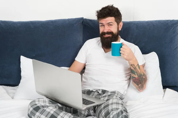 La matinée commence par le café et Internet. Homme d'affaires au lit. homme barbu travailler sur ordinateur portable et boire du café. mâle mature avec barbe en pyjama sur le lit. énergie et fatigue. homme d'affaires avec ordinateur — Photo