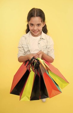 Alışveriş paketlerine bir bak. Bir sürü alışveriş torbası olan şirin bir çocuk. Kara Cuma indirimli. Alışveriş paketlerini alın. Kız alışveriş çantaları taşıyor. Sarı arka plan. Alışverişe düşkün kız