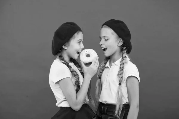 Godis butik och bageri koncept. Barn stora fans av bakade munkar. Dela sweet donut. Flickor i beret hattar håll glaserade donut röd bakgrund. Kids lekfulla flickor redo äter donut. Vänskap och generositet — Stockfoto